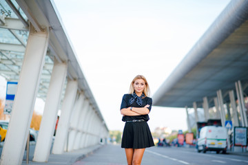 Portrait of young attractive blonde woman in black dress walking near the airport.