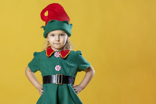 A little girl in the costume of a Christmas elf rests her hands on her hips. Near the blank place for text, copy space.