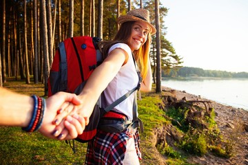 Portrait of happy young woman holding hand of her boyfriend while walking in forest.