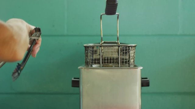 Woman placing and removing deviled crabs from deep fryer