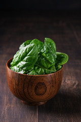 Fresh spinach in a wooden bowl on rustic wooden background, selective focus. Vertical. Spase for text.