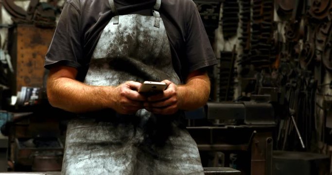 Blacksmith using mobile phone in workshop 4k