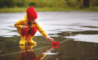 happy child girl with paper boat in puddle in autumn on nature