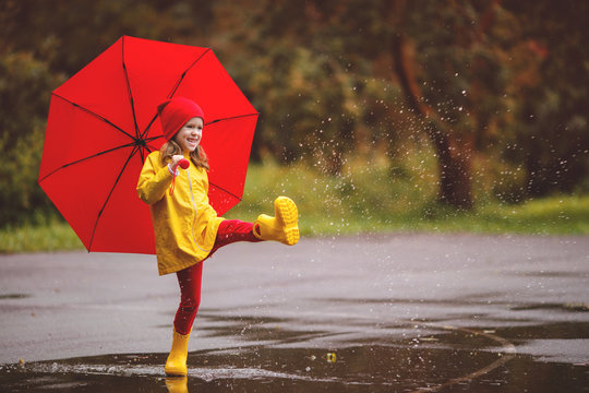 happy child girl with an umbrella and rubber boots jump in puddle  on autumn walk.