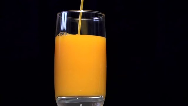 Pouring orange and yellow juice into a glass beaker. Behind the black background. A thin stream of juice is poured into a glass. Orange juice, pumpkin juice, mango juice, multifruit juice. 24 FPS