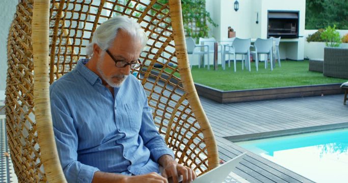 Senior man reading a book while sitting on hanging chair 4k