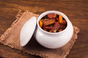 Stewed meat stew with vegetables, linen napkin on wooden background.