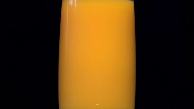 Pouring orange and yellow juice into a glass beaker. Behind the black background. A thin stream of juice is poured into a glass. Orange juice, pumpkin juice, mango juice, multifruit juice. 25 FPS