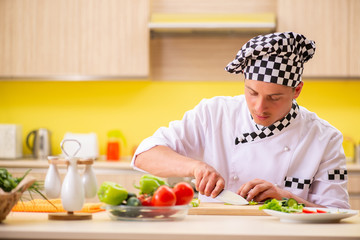 Young professional cook preparing salad at kitchen