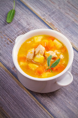 Chicken, butternut squash, apple, ginger and sage stew in white bowl on wooden table. Pumpkin soup with chicken. vertical