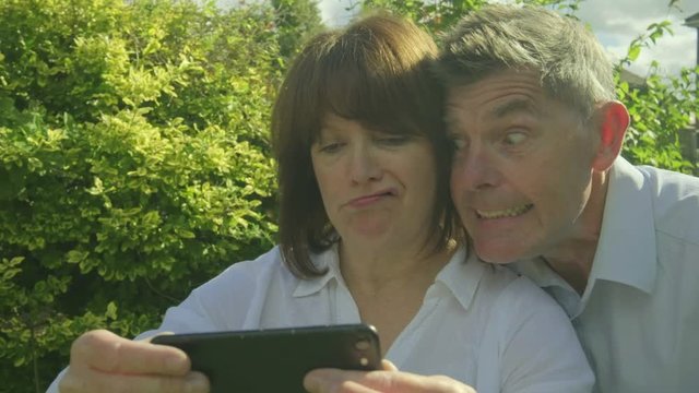 Senior caucasian couple taking selfies and making funny faces on a  smartphone in their garden