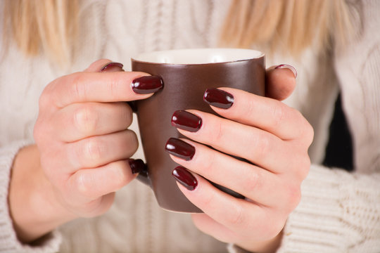 Girl with cup of coffee and brown nails polish. Woman wears beautiful sweater. Manicure and autumn concept. Close up, selective focus