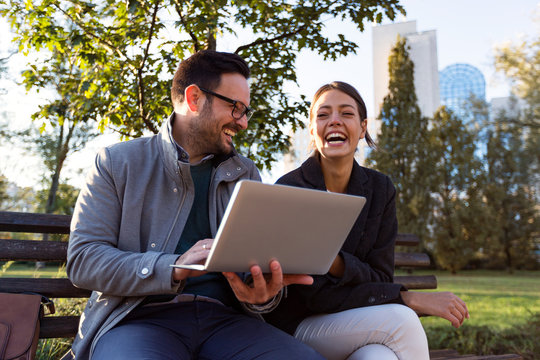 Business People Working On Laptop And Sitting On Bench In Park