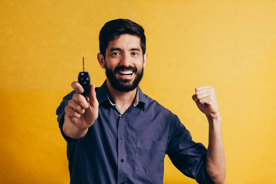 Portrait of young man smiling and holding car keys. Isolated yellow background