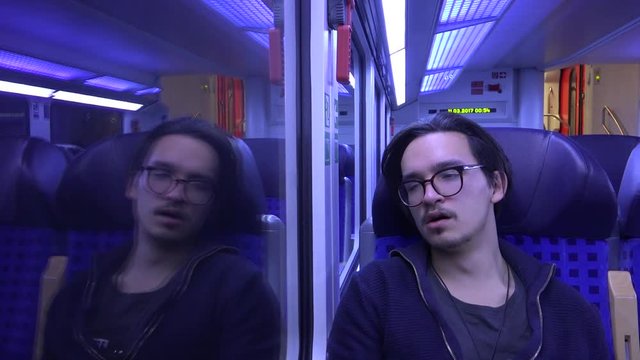 A young man yawning in a German train at night, almost falling asleep.