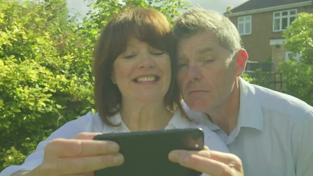 Senior caucasian couple taking selfies and making funny faces on a  smartphone in their garden