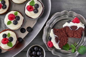 Chocolate muffins or cupcakes with whipped cream and berries in metal dishes