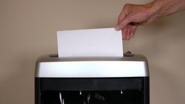 Static shot of mans hand shredding a paper vote into a shredder in front of office wall