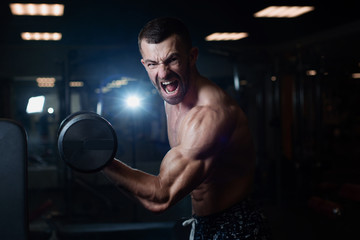 Fototapeta na wymiar young muscular man exercising with dumbbells. Guy trains his bicep