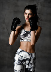 Fototapeta premium Young beautiful woman box trainer boxing in black gloves on concrete loft wall background
