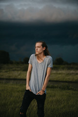 Obraz premium Attractive Young Male Model with Man Bun and Long Blonde Hair Posing for Camera Outside in Filed During Sunset