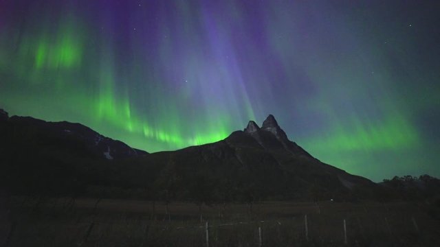 Real time video of Northern Lights or Aurora Borealis dancing in a clear night skies over a mountain. This is a rare case of so called corona with greens, purple and blue colours.