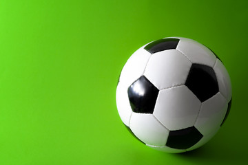 Sports equipment and leisure activity concept with a black and white generic classic leather football or soccer ball isolated on green background with copy space