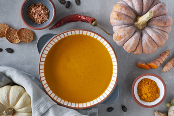 Pumpkin creme soup in stripy ceramic bowl surrounded by ingredients, text space
