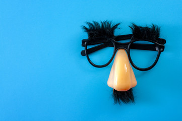 Happy april fool's day and funny pranks concept with a pair of comical glasses with bushy eyebrows and thick mustache isolated on blue background with copy space