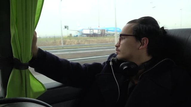 A young asian european man watches out of the flixxbus, while he passes the Schiphol Airport.