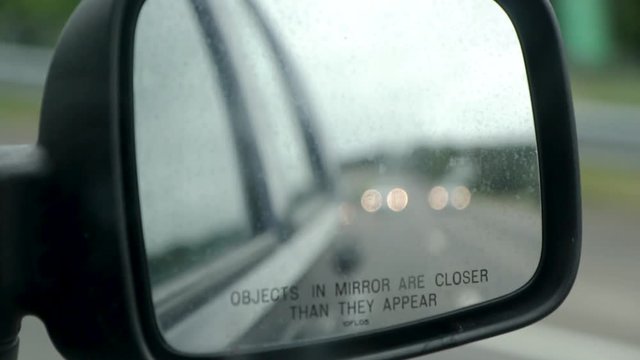 Close up video of a dirty side view car mirror from inside the car while driving with a blurry background