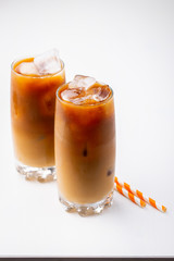 Ice coffee in a tall glass with cream poured over and coffee beans. Cold summer drink on white background with copy space
