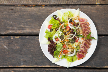 Close up of rare seared tuna slices with fresh vegetable salad on a plate with wood background