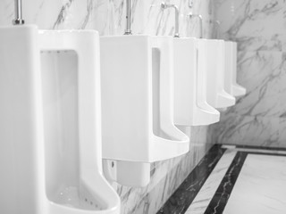 Row of clean white ceramic urinal chamber pot in marble wall in public men restroom.
