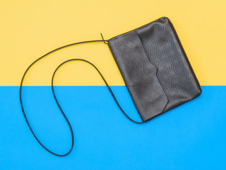 Leather black women bag on yellow and blue background. The view from the top. Flat lay.