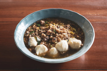 Thai-style hot and spicy soup noodles with meatballs and green vegetable condiment dressings in a blue bowl on a restaurant table