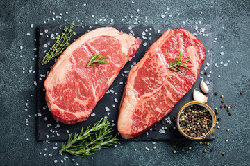 Fresh raw Prime Black Angus beef steaks on stone board: Striploin, Rib Eye. Top view. On a dark background