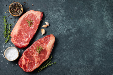 Fresh raw Prime Black Angus beef steaks on stone board: Striploin, Rib Eye. Top view with copy...