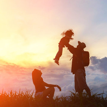 The happy family of three people, mother, father and child in front of a sunset sky.