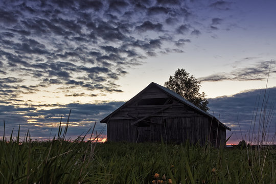 Midsummer Sun Sets Behind An Old Barn House