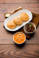 Suji/Sooji Halwa Puri or Shira Poori with black chana masala breakfast, served in a plate and bowl. selective focus