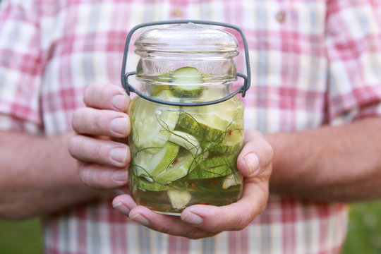 Man holding refrigerator cucumber pickles in a jar outdoors