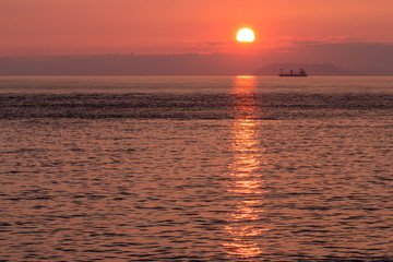 Silhouette of barge in ocean at pink sunset