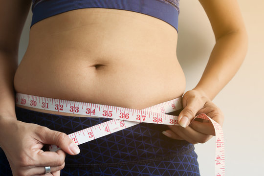 Woman hand holding measuring tape on belly fat