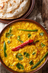 Lentil soup Dal Tadka with naan bread in a ceramic bowl on a wooden background. Vertical top view