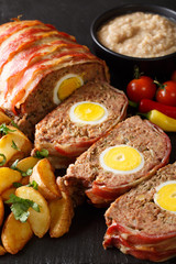 Hackbraten Meat loaf with egg served with potato wedges and sauce close-up on a slate plate. vertical