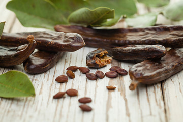 Carob pods with seeds and leaves on white wooden table. Healthy eating, food background.