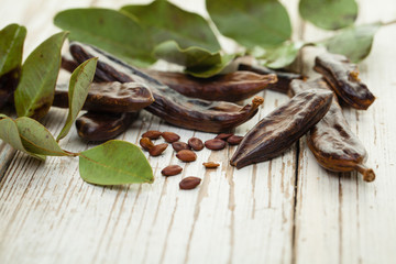 Carob. Healthy organic sweet carob pods with seeds and green leaves on a wooden board. Healthy eating, food background.