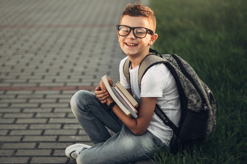 Obraz premium Portrait of a Little Boy in White T-Shirt and Jeans Holding Books in Hands Outdoors