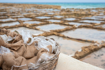 Salinas. Salt Pans or salters at the background with salt bags ready for sale in a basket or bowl outdoor. Hand harvest salt in Gozo Island Marsalforn. space for text.